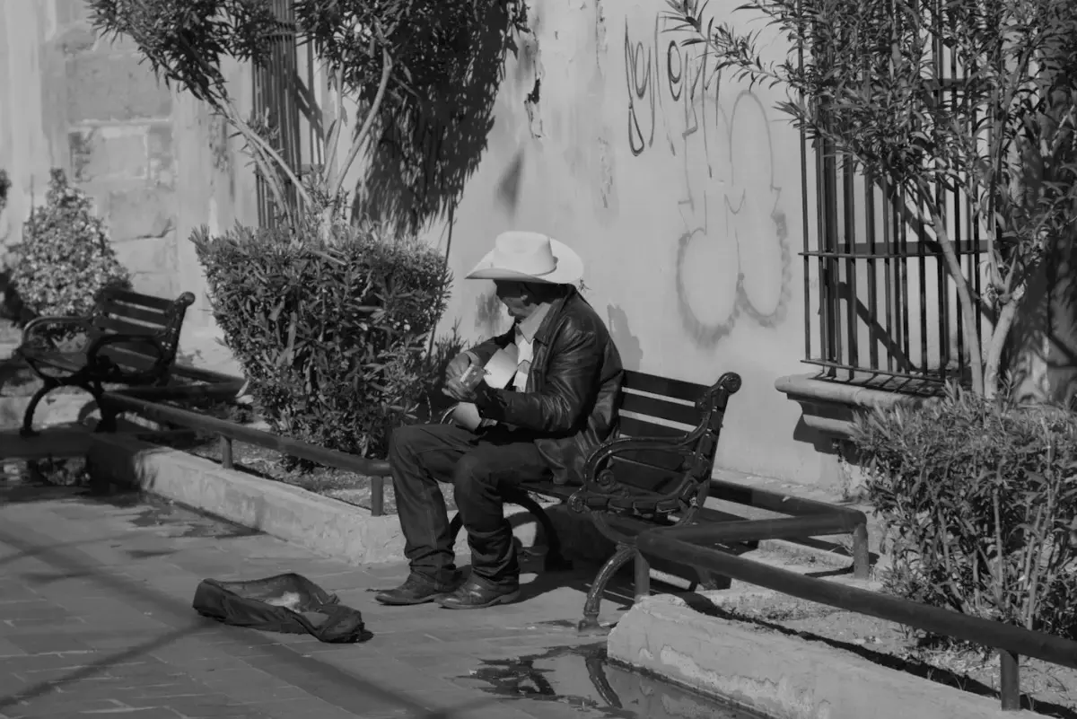 Un hombre con sombrero toca la guitarra en una banca del parque